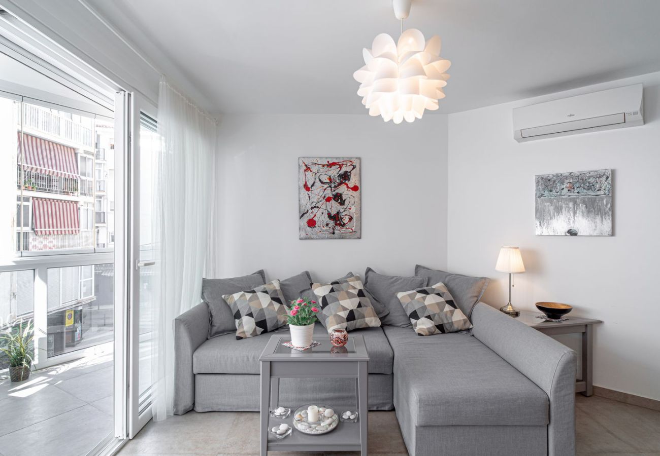 Salón luminoso con sofá de diseño y acceso directo a balcón acristalado en el centro de Nerja.